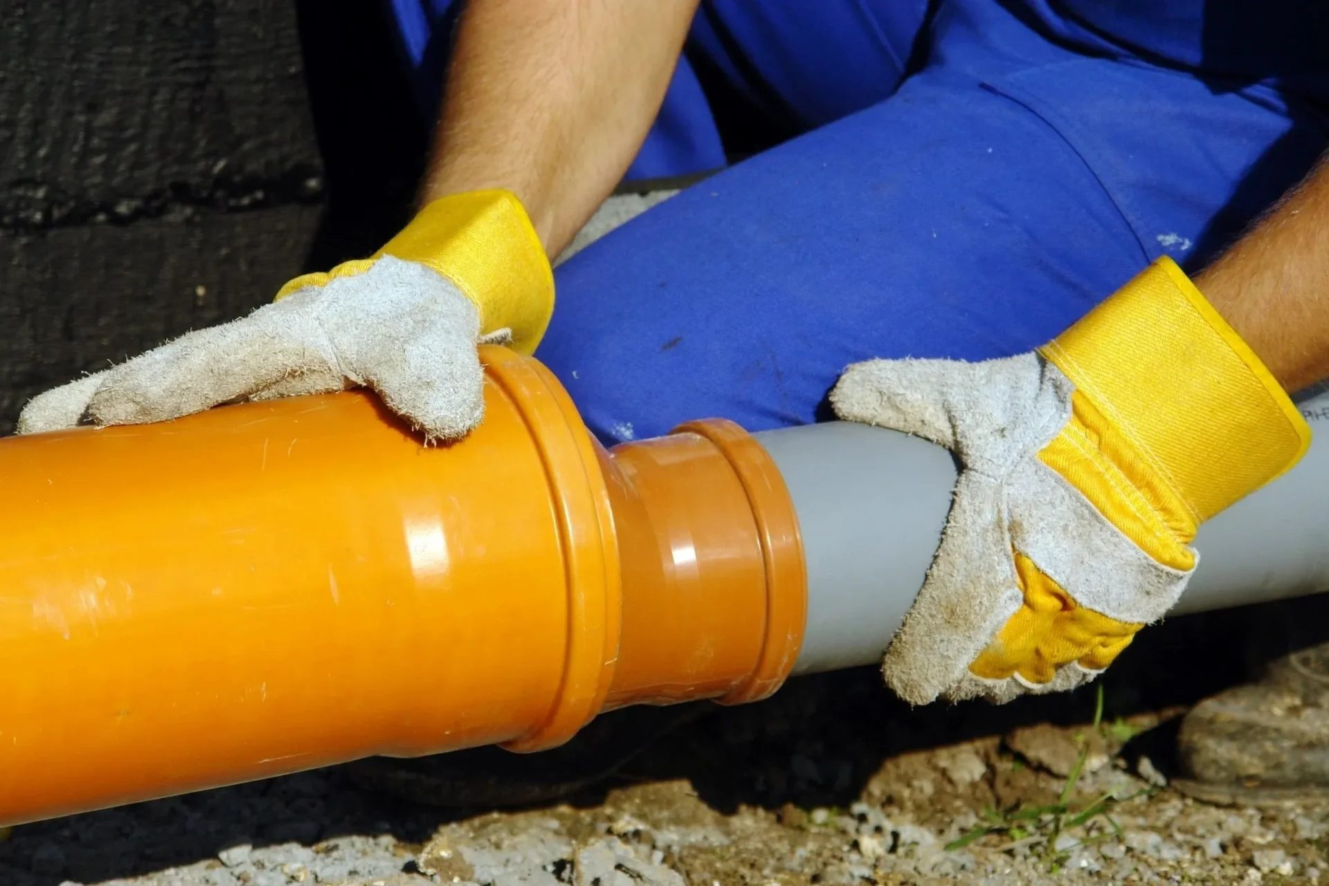 A person in blue shirt and yellow gloves holding orange pipe.